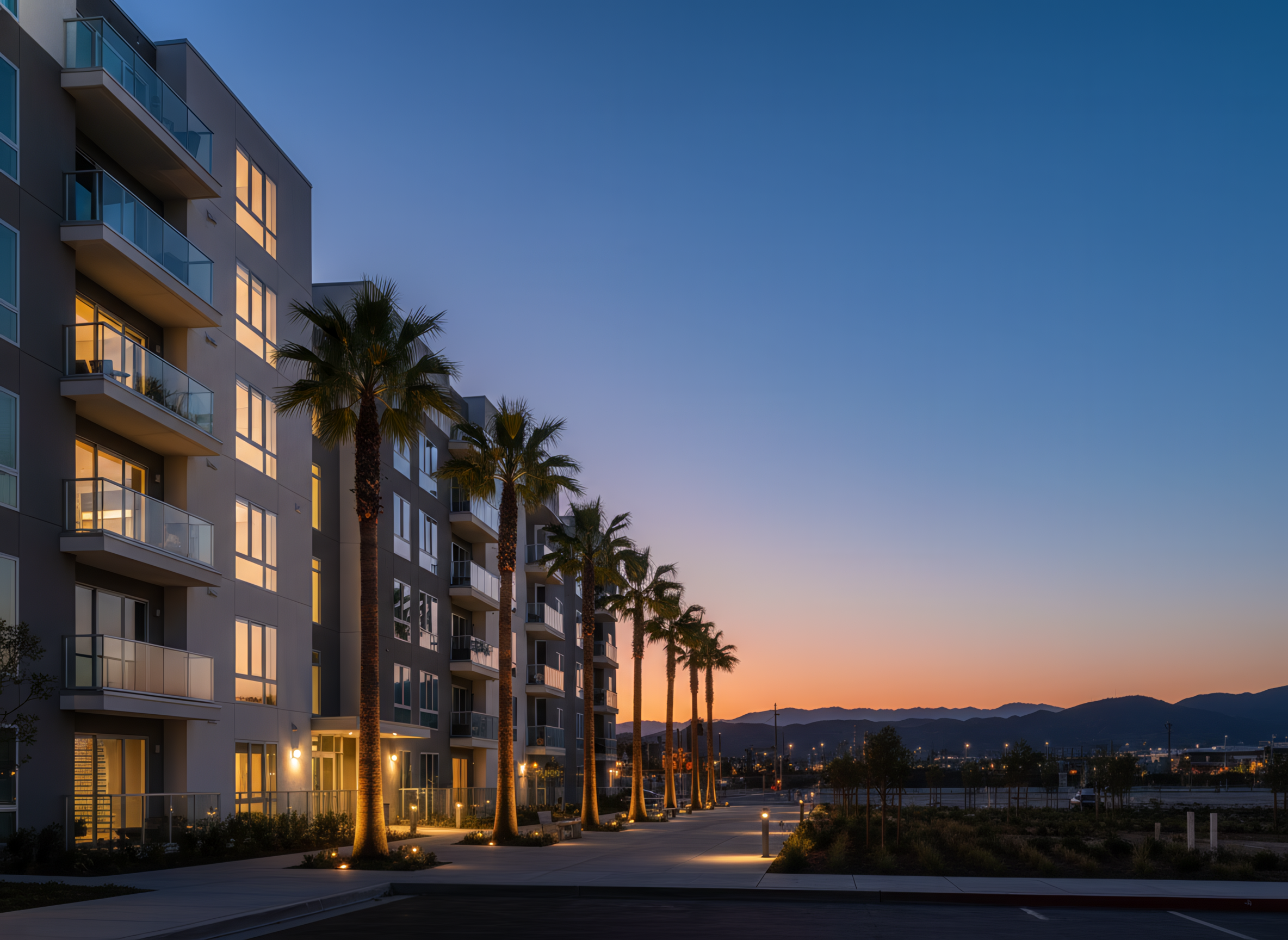 California multifamily housing at sunset with illuminated windows, palm trees, and distant hills